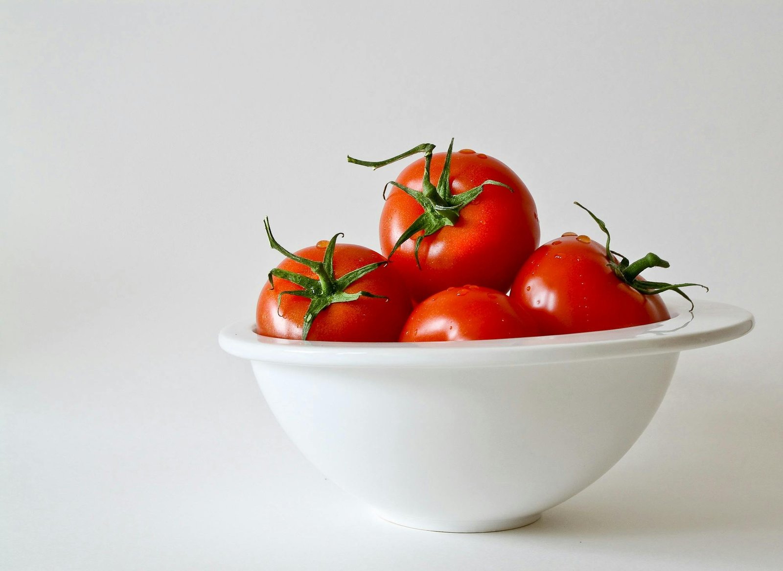 Vibrant red tomatoes in a white bowl, emphasizing freshness and simplicity.